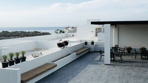 Une terrasse sur le toit offrant une vue sur la mer, avec un espace salon agrémenté de coussins et de plantes en pot.