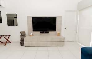 A modern living room with a large flat-screen TV mounted on a light wood cabinet, a small side table with a basket, and a blue armchair.