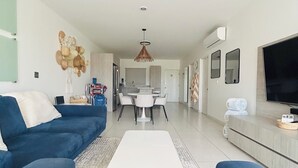 Un salon moderne avec un canapé bleu, une table basse blanche et un coin repas comprenant une table et des chaises blanches.