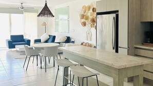 Une cuisine moderne dotée d’un îlot central, de tabourets de bar, d’un réfrigérateur et d’un coin repas avec un canapé bleu et des chaises blanches.