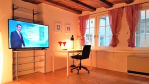 A room with a wooden ceiling, a desk with a chair, a TV displaying a weather forecast, and a window with checkered curtains. - CHALET AU SWISS style (Zürich)