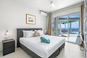 A modern hotel room with a large bed, a nightstand, a framed picture, and a view of the ocean.