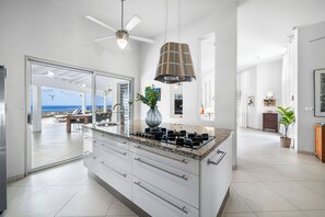 A modern kitchen with a large island, a ceiling fan, and a view to an outdoor area.