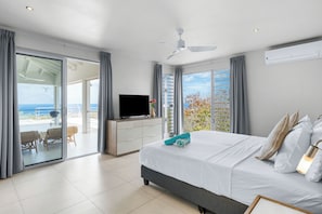 A bedroom with a bed, a TV, a balcony with a view, and a ceiling fan.