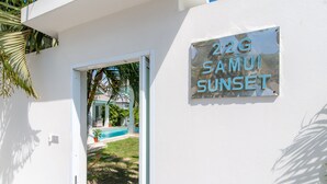 A white building with a sign reading "202G SAMUI SUNSET".