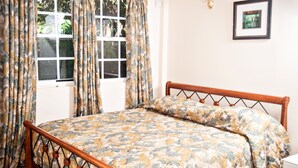 Ein Schlafzimmer mit einem blumengemusterten Bettbezug, einem Holzkopfstück und einem Fenster mit Vorhängen.
