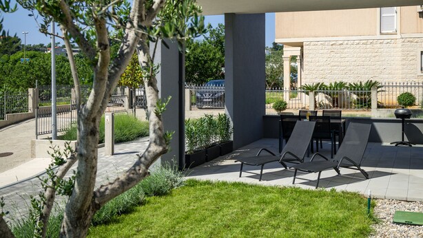 Un espace extérieur moderne aménagé avec des sièges, une balustrade en verre, un arbre et un bâtiment en arrière-plan.