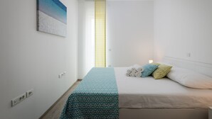 Une chambre à coucher comprenant un lit, une table de chevet, un tableau accroché au mur et une fenêtre avec un store à motifs.