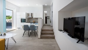 Une cuisine moderne avec des meubles blancs, un four encastré et un coin repas gris avec des chaises.