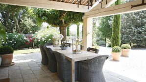 An outdoor patio with a long dining table, wicker chairs, and potted plants.