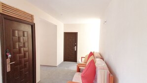 Un pasillo con una puerta de madera a la izquierda, una cama con almohadas a la derecha y una pared lisa.