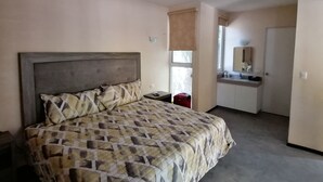 Un dormitorio con cama, ventilador de techo, ventana con vistas, baño con lavamanos y una puerta.