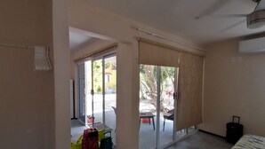 Una habitación de hotel con una puerta corrediza de vidrio que da a un patio, una cama, una maleta y una pequeña mesa con una silla.