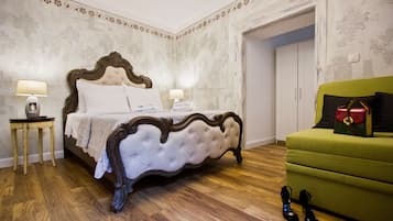 A bedroom with a large bed, two bedside tables with lamps, a green armchair, and a pair of shoes on the floor.