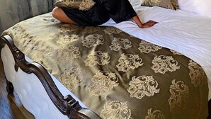 Une personne assise sur un lit doté d’une tête de lit décorative, d’un lustre et de rideaux à motifs.