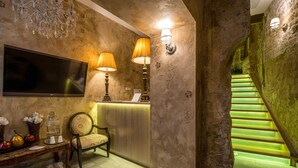 Un espace d’accueil doté d’un téléviseur à écran plat, de deux lampes fixées au mur, d’un comptoir de réception, d’une chaise et d’un escalier éclairé de lumière verte.