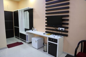 Habitación compacta con kitchenette, un refrigerador pequeño, un basurero, un escritorio con computadora y un televisor montado en la pared.