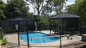 Una piscina cercada con un área de estar cubierta y un pabellón.