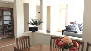 Un comedor con una mesa y sillas de madera, un florero con flores y vistas a una sala de estar a través de un arco abierto.