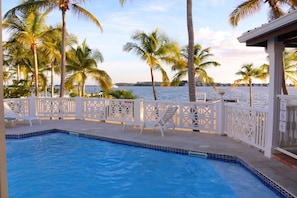 A swimming pool with white chairs, surrounded by palm trees and a view of the sea. - le "Madras Blue" Duplex, Baie Nettlé, piscine-vue (Marigot)