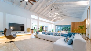 A spacious living room with a large white sofa, a modern chair, and a flat-screen TV. - Luxury Villa: 6 Rooms, 12 Pax, Infinity Pool, Hot Tub, Staff, Close to the Beach (La Romana)