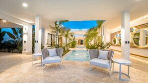 A modern indoor pool area with two white lounge chairs, a small pool, and tropical plants. - Luxury Villa: 6 Rooms, 12 Pax, Infinity Pool, Hot Tub, Staff, Close to the Beach (La Romana)