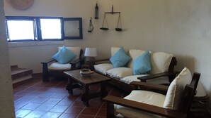 Una sala de estar con un sofá, dos sillones, una mesa de centro, una lámpara y una báscula fijada a la pared.