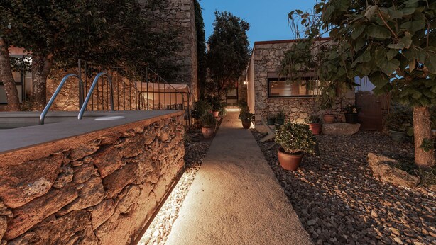 Un camí de pedra que condueix a un edifici amb barana metàl·lica i plantes en testos.