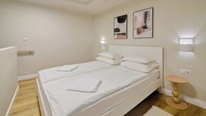Een tweepersoonsbed met witte lakens, een nachtkastje en twee wandlampen.