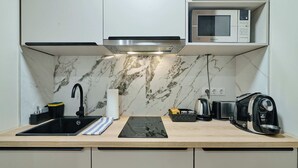 Een moderne keuken met een ingebouwde magnetron, een zwart inductiekookplaatje, een spoelbak en een koffiezetapparaat.