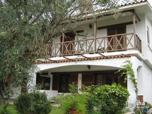 Um edifício de dois andares com varanda, cercado por vegetação.