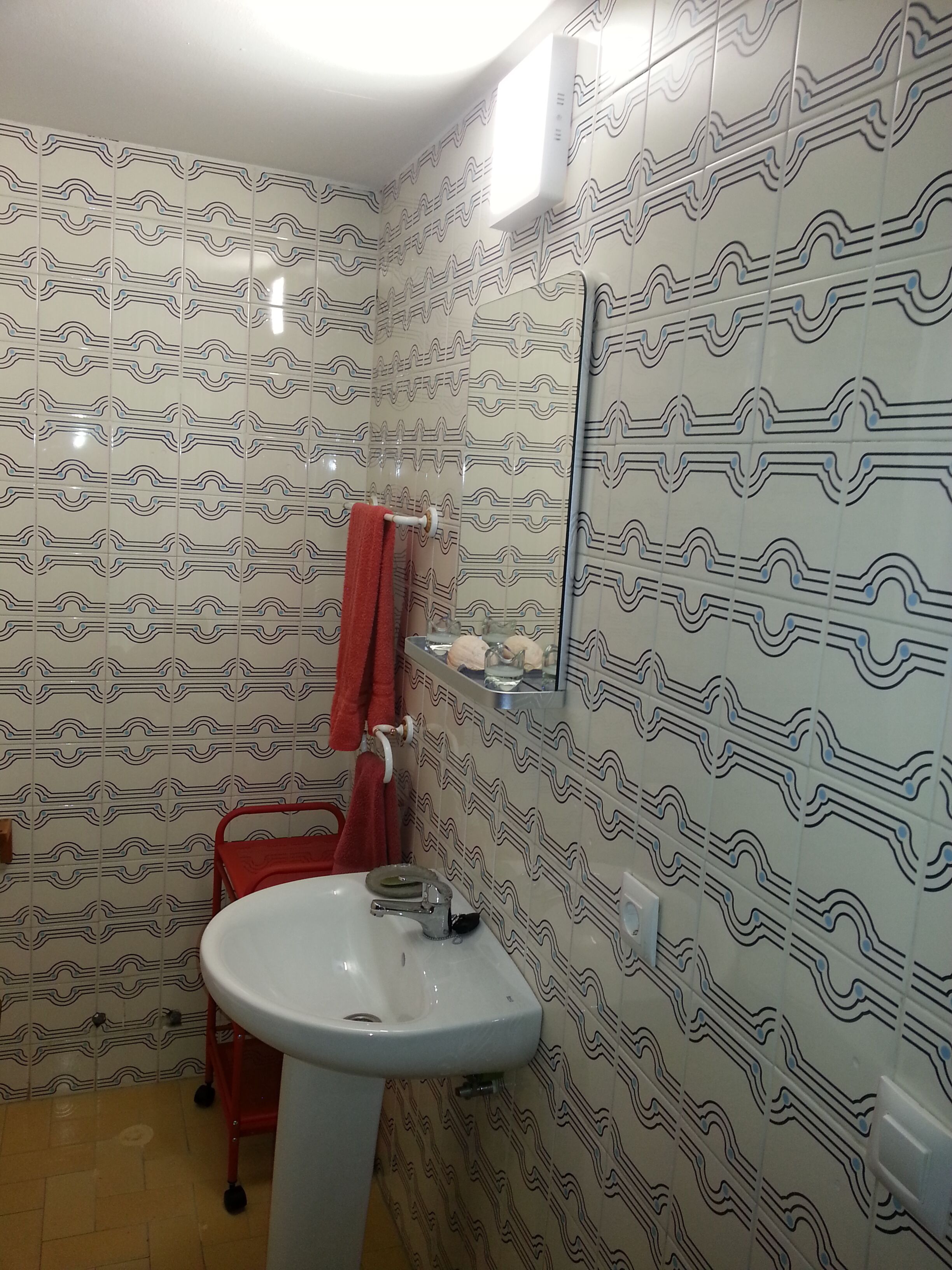 A bathroom with patterned tiles, a white sink, a red chair, and a towel rack.
