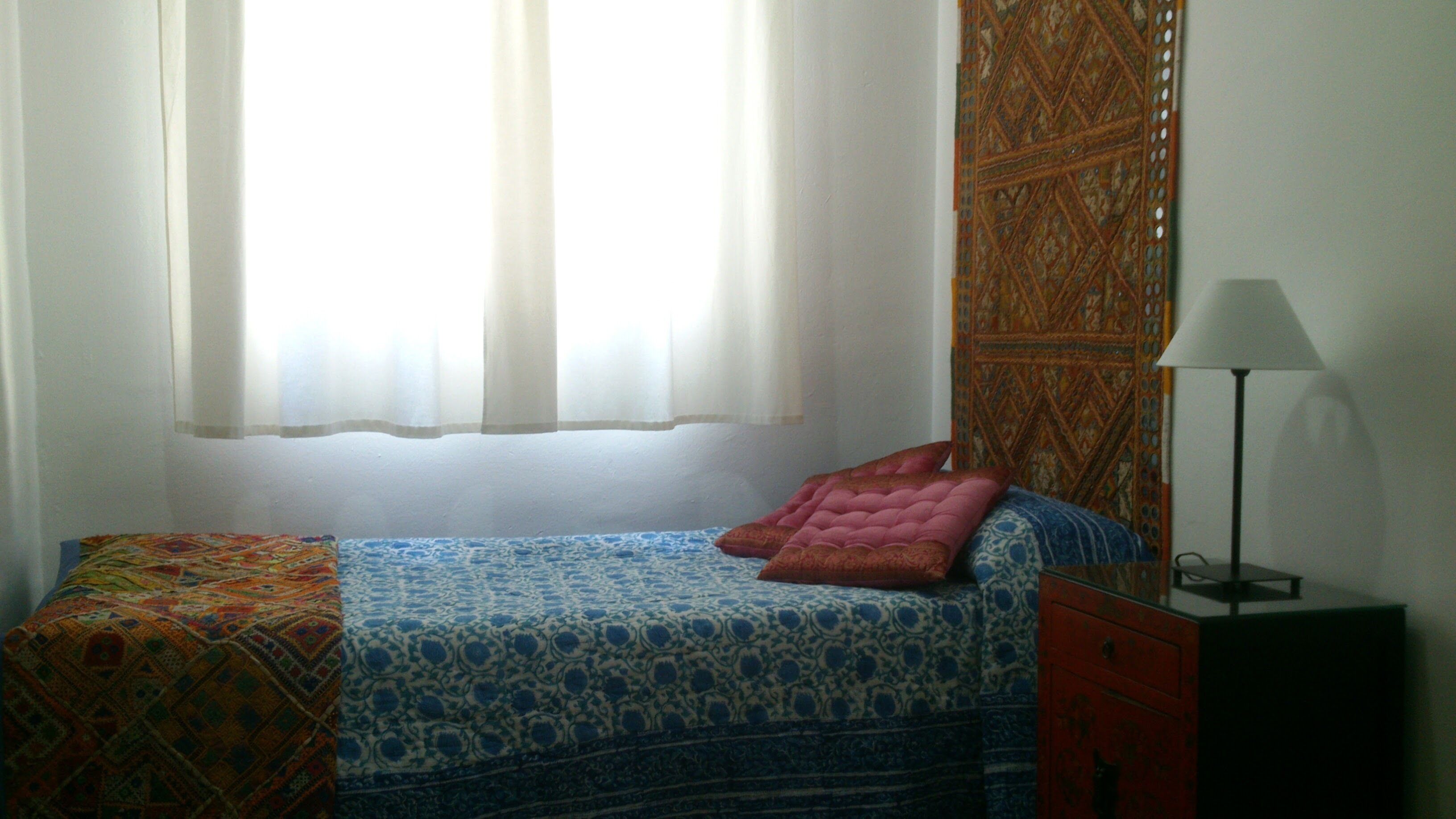 Une chambre à coucher avec un lit, une table de chevet, une lampe et un mur décoré d’un motif.
