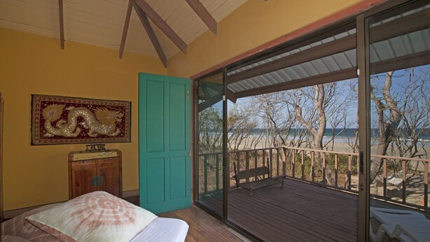 Een slaapkamer met een bed, een houten kast, een groene deur en een groot raam met uitzicht op een strand.