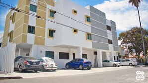 Un edificio moderno de varios pisos con fachada plana, varias ventanas y un estacionamiento con automóviles.