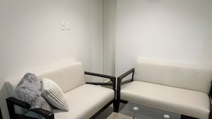 Una sala de estar moderna con dos sofás, una mesa de centro de vidrio y una silla de madera oscura.