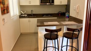 Una cocina compacta con armarios blancos, un microondas de acero inoxidable, un lavamanos y una encimera con dos taburetes.