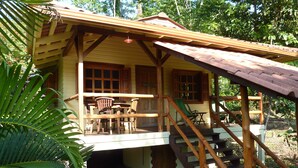 Une cabane en bois avec une véranda, une table à manger avec des chaises et un escalier menant au bâtiment principal.