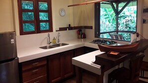 Une cuisine équipée d’un évier à deux bacs, d’une cuisinière, de meubles en bois, d’une fenêtre donnant sur un espace verdoyant et d’une horloge murale.
