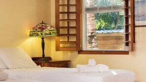 A bedroom with a bed, a nightstand, a lamp, a window with a view of trees, and a towel on the bed. - Cozy Two Twin Bed Suite (Orchid Bay)