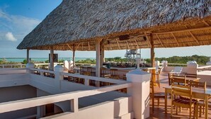 A rooftop terrace with a thatched roof, outdoor seating, and a view of the ocean. - Cozy Two Twin Bed Suite (Orchid Bay)