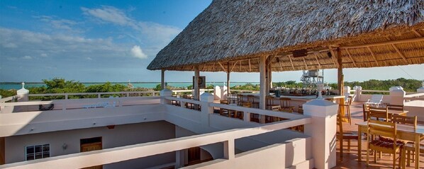 A rooftop terrace with a thatched roof, outdoor seating, and a view of the ocean. - Cozy Two Twin Bed Suite (Orchid Bay)
