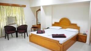 A bedroom with a wooden bed, two chairs, a nightstand, a mirror, and a window with curtains.
