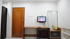 A room with a wooden desk, a chair, a television mounted on the wall, a mirror, and a door.