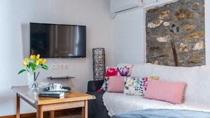 A modern living room with a flat-screen TV, a wooden coffee table, a sofa with colorful cushions, and a stone wall. - Large Villa for nine people (Skopelos Town, Skopelos Island)
