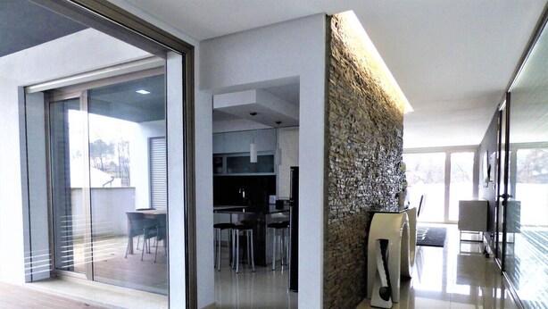 A modern interior with a glass door leading to an outdoor area, a kitchen with white cabinets, and a stone accent wall. - Beautiful house ideal for relaxation (Bela Monção)