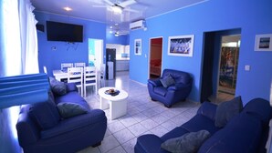 Ein Wohnzimmer mit blauen Sofas, einem weißen Couchtisch und einem an der Wand befestigten Fernseher.