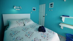 Ein Schlafzimmer mit einem Bett, einer Tür, einer Wand-Klimaanlage, einer Wandleuchte, einem kleinen Bild und einem blauen Korb.
