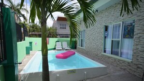 Ein Swimmingpool mit einem rosa Schwimmer, umgeben von einem grünen Zaun und einer Steinmauer.