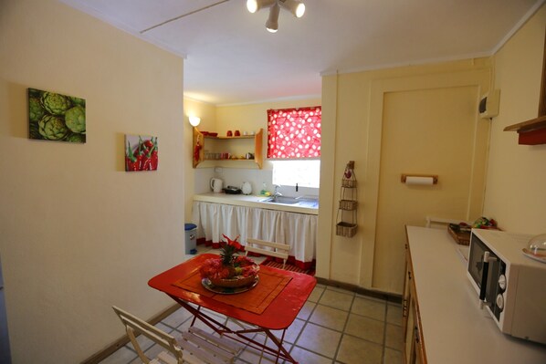 A compact kitchen with a dining table, a microwave, and a window with red curtains.
